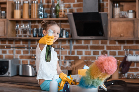 girl with spray bottle and different cleaning supplies at home