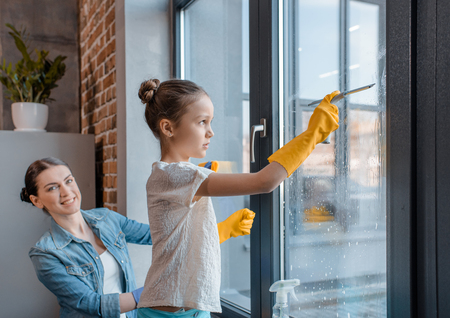 mother and cute little daughter in protective gloves cleaning window togetherの写真素材