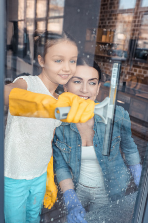 mother and daughter in protective gloves cleaning window togetherの写真素材