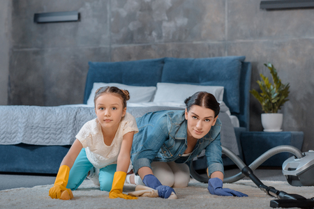 Mother and cute little daughter cleaning carpetの写真素材