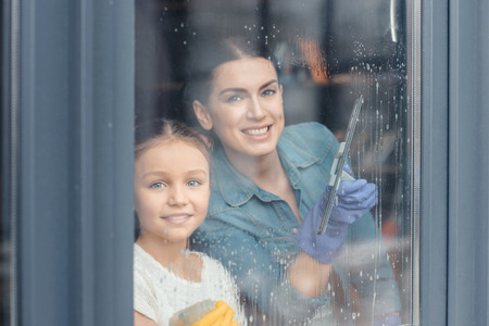 mother and daughter cleaning window and smiling at cameraの写真素材