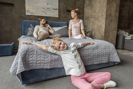 adorable daughter with mother and father relaxing on bed at homeの写真素材