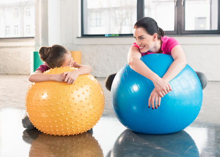 mother and daughter lying on fitness balls and smiling each otherの写真素材