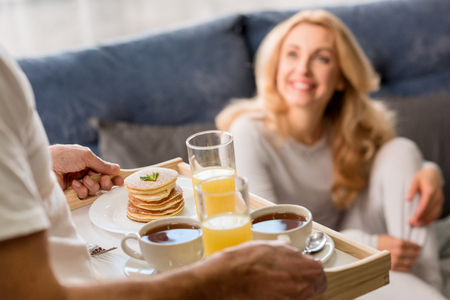Man bringing tray with tasty breakfast to happy blonde womanの写真素材