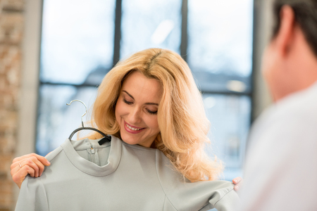 blonde middle aged woman trying on grey fashionable dress indoorsの写真素材