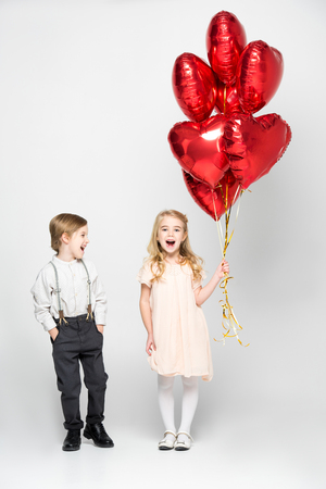 Excited little boy looking at cute girl while she holding heart shaped air balloonsの写真素材