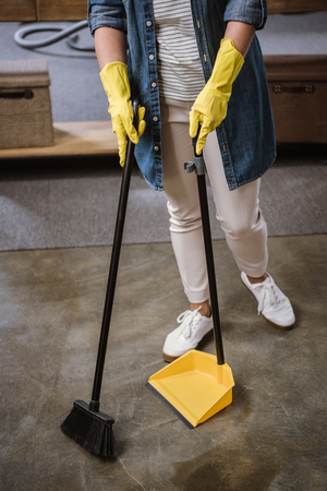 Partial view of woman in gloves sweeping floor with broom and dustpanの写真素材