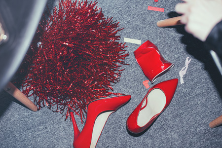 Close-up view of red fashionable high-heeled shoes on messy floor after party
