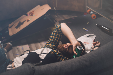Drunk bearded young man sleeping on couch with bra and beer canの写真素材
