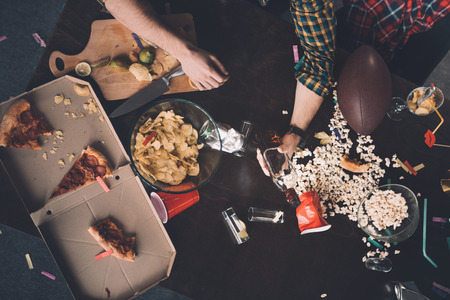 man holding whiskey bottle at messy table after partyの写真素材