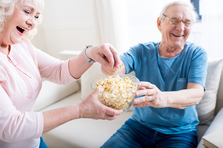 couple eating popcorn and sitting on sofa at homeの写真素材