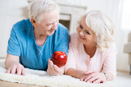 senior couple lying on carpet with big red appleの写真素材