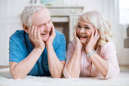 senior couple lying on carpet and smiling each otherの写真素材