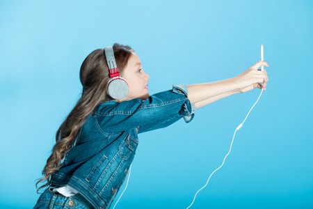 little girl in headphones using smartphone in studio on blueの写真素材