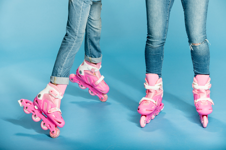 low section of mother and daughter in roller skates in studio on blue