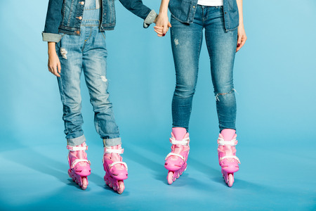 mother and daughter in roller skates holding hands in studio on blue
