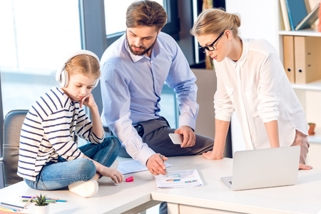 businesswoman and businessman working with documents and laptop while daughter sitting with headphonesの写真素材