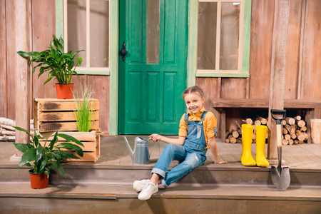 smiling little girl sitting on porch with watering canの写真素材
