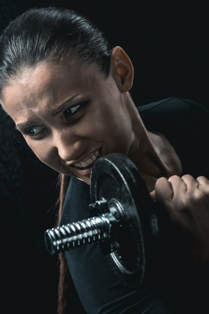 young fitness woman training with dumbbells isolated on black.の写真素材