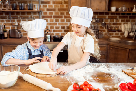 children making pizza dough with pizza ingredients on foregroundの写真素材