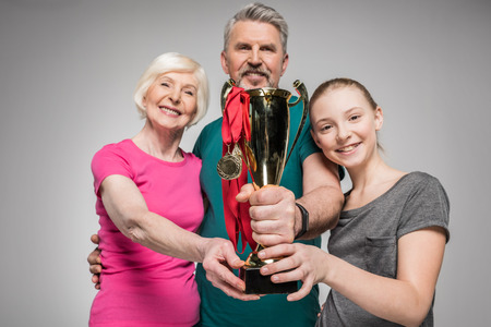 Happy old couple and girl holding sport trophy and medalsの写真素材