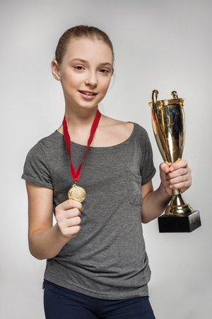 Smiling girl in sportswear holding trophy and medalの写真素材