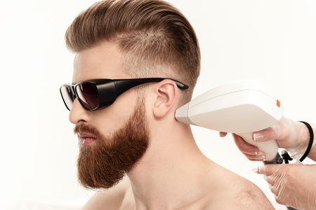 young man receiving laser skin care on neck isolated on whiteの写真素材