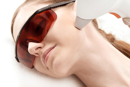 young woman in uv protective glasses receiving laser skin care on faceの写真素材