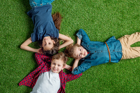 three cute kids lying on grass with hands behind heads and smilingの写真素材