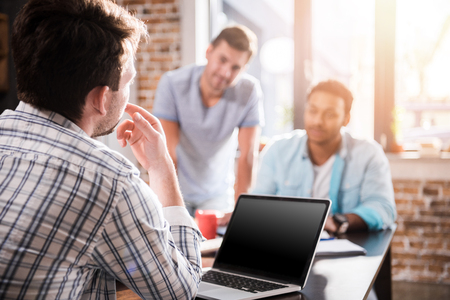 man using laptop while colleagues discussing project, small business meeting conceptの写真素材