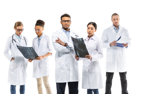 Team of young professional doctors in white coats standing together isolated on whiteの写真素材