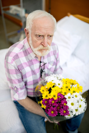 Senior man with flowers in hospitalの写真素材