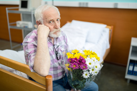 Senior man with flowers in hospitalの写真素材