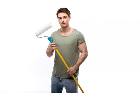 handsome man holding paint roller and looking at camera isolated on whiteの写真素材