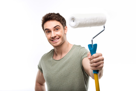 handsome man holding paint roller and looking at camera isolated on white