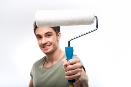 handsome man holding paint roller and looking at camera isolated on whiteの写真素材