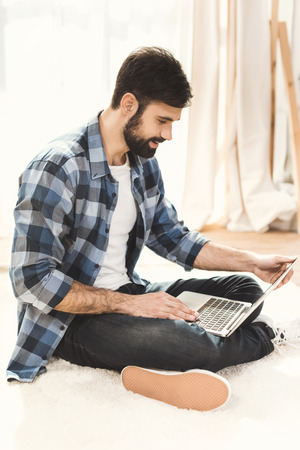 Man sitting on carpet and working on laptopの写真素材