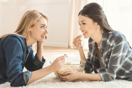 women lying on carpet and eating popcornの写真素材
