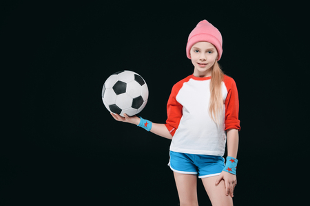 Cute girl in sportswear posing with soccer ball isolated on blackの写真素材