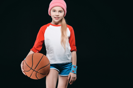 Cute girl in sportswear posing with basketball ball isolated on blackの写真素材