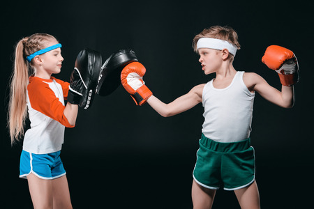 Side view of boy and girl in sportswear boxing isolated on blackの写真素材