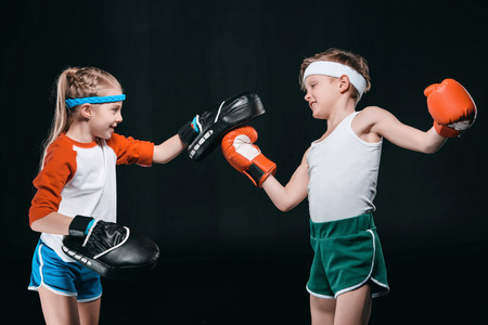 Side view of boy and girl in sportswear boxing isolated on blackの写真素材