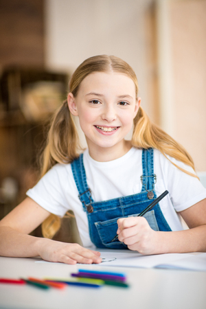little girl drawing at table and smiling at cameraの写真素材