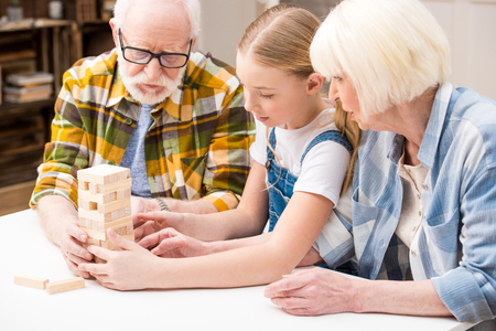 little girl with grandparents playing jenga game together at homeの写真素材