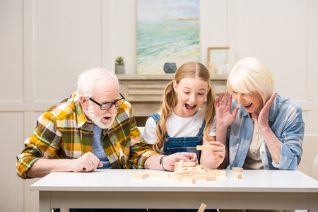 preteen girl with grandfather and grandmother playing jenga game at homeの写真素材