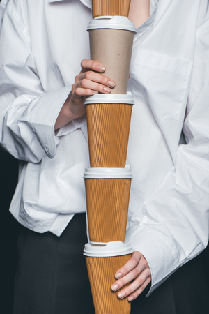 Mid section of woman holding a pile of disposable coffee cups, studio shotの写真素材