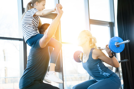 Woman workout with barbell while man having fun with daughter on his shouldersの写真素材