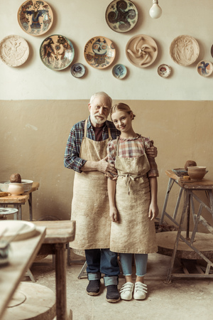 senior potter with his granddaughter in aprons standing at workshopの写真素材