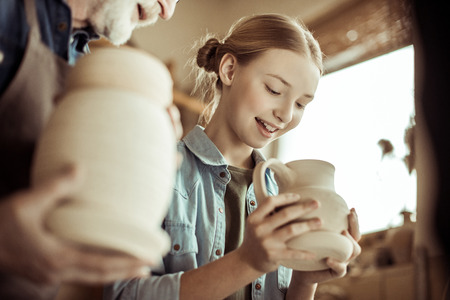 Granddaughter and grandfather holding and examining clay goodsの写真素材