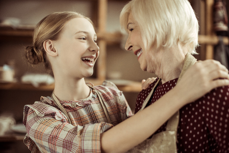 Granddaughter hugging her grandmother while they standing in apronsの写真素材